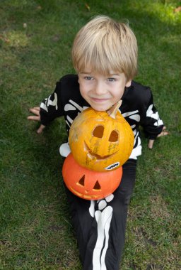 İskelet bir kostüm giymiş, kabak oyulmuş, yukarı bakıp gülümseyen bir çocuğun portresi. Cadılar Bayramı