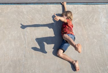 Yalınayak çocuk asfaltta komik bir gölge yapıyor, yerde yatıyor ve baş parmağını kaldırıyor. İlginç bir çocukluk, hayal gücünü geliştirme, gölgelerle oynama.