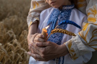 Buğday tarlaları arasında Ukraynalı anne ve oğulun ellerinde sarı-mavi renklerle boyanmış mum ve iki buğday kulağı. Ukrayna 'daki Holodomor sırasında ölenlerin anısına Spikelet ve ateş