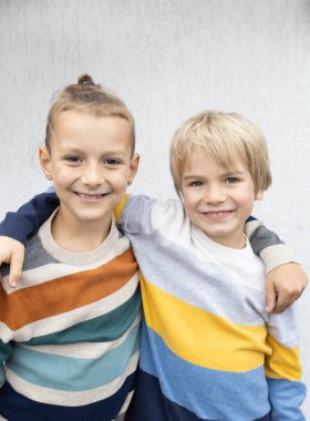 7 yaşındaki çizgili kazaklı iki kardeş ya da arkadaş mutlu bir şekilde sarılıyor. İletişim zevki, tatilden sonra sınıf arkadaşlarının neşeli buluşması. çocukluk