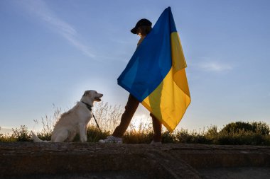 Gün batımında sırtında Ukrayna bayrağını tutan bir kadının köpeğinin silüeti. Ukrayna 'nın Bağımsızlık Günü. Özgürlük, güven, gurur, ulusal sembol