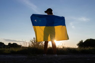 Gökyüzüne ve batan güneşe karşı Ukrayna bayrağı tutan bir kadının silueti. Ukrayna 'nın Bağımsızlık Günü. Özgürlük, gurur, ulusal sembol. Ukrayna 'yı destekleyin. Ukraynalı olmaktan gurur duyuyorum. Savaşı durdurun.