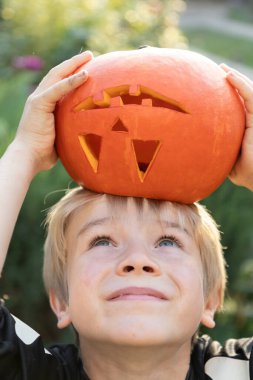 Çocuk kafasına portakal oymalı bir balkabağı yerleştirdi. Cadılar Bayramı için hazırlanıyorum. Neşeli bir çocukluk, şımartıcı. Korkmayın, eğlenin.