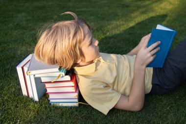 Çocuk kafası bir yığın kitabın üzerinde çimlerin üzerinde uzanıyor ve bir tanesini okuyor. Okumaya başla, okula dön, ilginç bir çocukluk geçir. Eğitim konsepti ve bilgi motivasyonu. kitap günü