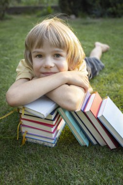 Tatlı çocuk başını çimlerin üzerinde yatarken bir yığın kitabın üzerine koydu. Okula dönüyorum. Kitap Günü. Zevkle okuyun. Eğitim, hayal gücünün gelişimi