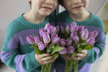 Aynanın yanındaki sevimli çocuğun pembe leylak rengi lalelerle dolu yüzünün bir parçası. Seçici odaklanma, yansıma. Çocukluğun şefkati. Kutlama havası, anneye sevgilerle hediye, anneanne. Anneler Günün kutlu olsun..
