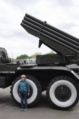 Genç çocuk askeri aracın yanında duruyor, çoklu fırlatma roketi sistemi. Rus işgali Ukrayna topraklarında. Ukrayna Silahlı Kuvvetleri 'nde Gurur. Savaşı durdurun. Kyiv 'de askeri teçhizat sergisi
