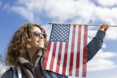 Güneş gözlüklü, elinde Amerikan bayrağı olan güzel, mutlu bir genç kadının yüz resmi. 4 Temmuz. Amerika Birleşik Devletleri 'nin Bağımsızlık Günü. Gurur, özgürlük. Mutluluğun samimi gülümsemesi