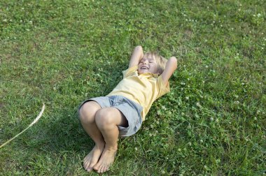 Mutlu çıplak ayaklı çocuk çimlerin üzerinde yatıyor, ayakları dikenle gıdıklanıyor. pozitif atmosfer, neşeli çocukluk. Merhaba yaz. Doğanın rahatlatıcı enerjisi. Dünya Günü. seçici odak