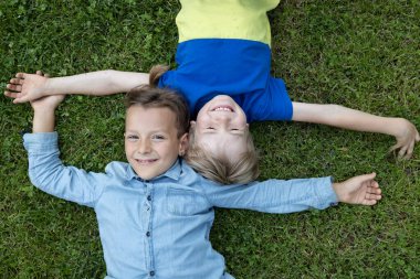 İki küçük çocuk çimlerin üzerinde sırt üstü yatıyor. Bir yaz parkında dinlenen neşeli çocuklar. Neşe, pozitiflik, birlikte eğlenceli zamanlar. Sonsuza dek arkadaşız. Arkadaşlarla tanışmak ve dışarıda oynamak.
