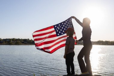 Çocuk ve bir kadın göle karşı bir gölün kenarında duruyor, rüzgarda dalgalanan bir Amerikan bayrağını tutuyorlar. Aile, birlik, özgürlük. Parlak gelecek