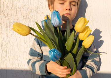 Bir buket sarı-mavi laleyle üzgün bir çocuğun portresi. Ukrayna 'yı destekleyin. Savaş sırasında mutsuz bir çocukluk. Ukrayna 'daki savaşı durdurun. Vatanseverlik, ulusal kimlik.