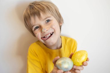 Yüzüne bir sürü renkli şeker serpiştirilmiş komik çocuk portresi, açık arkaplana yumurtalar çizmiş. Çocukların şımartılması, çocukluk sevinci. Paskalya için Hazırlık