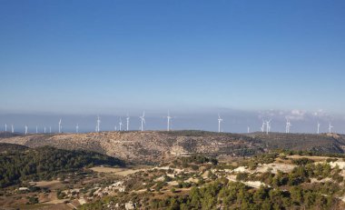 Güneşli bir günde mavi gökyüzüne karşı elektrik üretimi için sıra sıra rüzgar türbinleri. Doğanın ekolojik olarak temiz enerjisi. Kıbrıs 'ın Manzarası