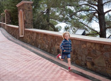 5-6 yaşındaki çocuk parkta neşeyle koşuyor, temiz havada spor yapıyor. Aktif oyun ve sağlıklı yaşam tarzı kavramı. Kim daha hızlı?