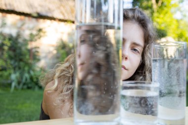 Camın içinden bir bardak suyun arkasından dışarı bakan çarpık bir kız yüzü. Bireysellik arayışı. Optik illüzyonlar, bölünmüş kişilik, iç sorunlar, endişeler, baş ağrısı, yorgunluk,