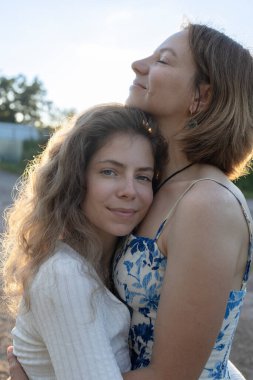 40 'lı yaşlarda mutlu bir annenin şehvetli portresi ve arka planda şefkatle sarılan yetişkin kızı. Nesiller arası yakınlık. Aile içinde destek ve sevgi. Anneler Günü. Kızların Günü