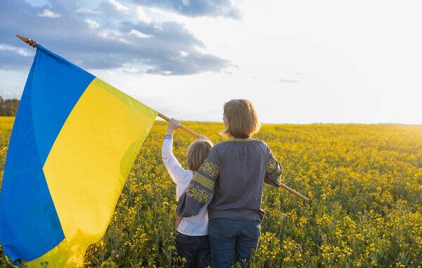 мальчик и женщина в традиционной вышитой рубашке, мать сына прижата вместе с флагом Украины среди рапсового поля. День независимости, патриотизм. Гордость быть украинцем. Встать на сторону Украины