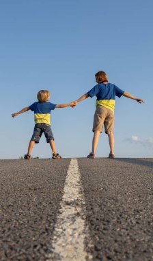 Sırtları havada asfalt yolda el ele tutuşan mavi tişörtlü bir erkek ve kadın. Aile, mülteciler, birlik, destek, parlak gelecek. Yaşasın Ukrayna. Ukraynalı olmaktan gurur duyuyorum.