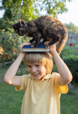 Kitap ve kedi yavrusu, neşeli ve komik 8 yaşındaki bir çocuğun kafasının üstünde oturuyor. Merhaba okul. Kitap günü. Hayvanlarla okumayı ve iletişim kurmayı seviyorum. Dijital detoks. Çocuk oyunları, ilginç bir çocukluk.