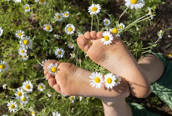 Vahşi papatyaların arasında çıplak ayaklı bir çocuk, yakın plan. Mutlu çocukluk, pozitif düşünce, yaz havası, mutlu tatiller. Dünya Günü. Ayak sağlığı