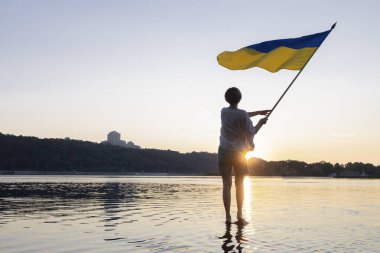 Kadın, günbatımında Dinyeper Nehri 'nde dururken elinde büyük sarı ve mavi bir Ukrayna bayrağı sallıyor. Ukraynalı olmaktan gurur duyuyorum. Bağımsızlık Günü. Zafere olan inanç. Savaşı durdurun. Anavatan