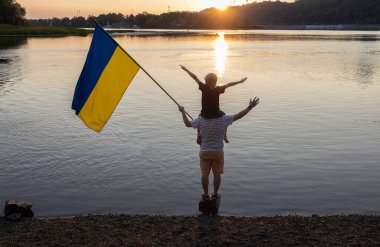 Ukraynalı olmanın gururu, Ukrayna 'nın zaferine olan inancı. Bağımsızlık Günü. Omuzlarında büyük bir Ukrayna bayrağıyla gün batımında Dinyeper Nehri yakınlarında oturan oğlu olan baba. Vatansever eğitim.