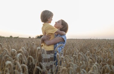 Kadın ve çocuk, buğday tarlasında buğday başakları arasında kucaklaşan anne ve oğul. Aile, mülteciler, birlik, destek, birliktelik. Ukrayna 'yı destekleyin. Anneler Günü. Oğullar Günü. Gerçek insanlar.
