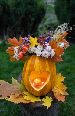 Sonbahar yaprakları ve çiçekleri bir vazo gibi balkabağının içinde duran kesilmiş bir kalbin içinde yanan mum. Doğal sonbahar malzemelerinden DIY dekor