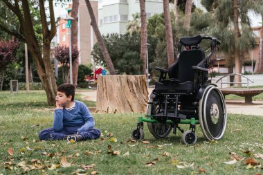 Child with a disability relaxing sitting on a grass in a public park. People with a disability.
