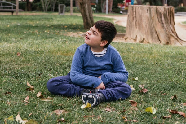 Kid with multiple disabilities relaxing outdoors sitting on a grass in a park. People with a disability.