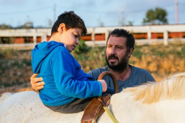Disabled Child performing upper trunk exercises during equine therapy with the assistance of a physiotherapist