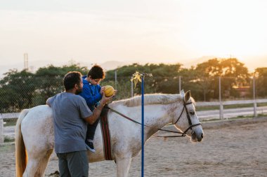 Physiotherapist using a ball during an equine therapy session with a child with cerebral palsy