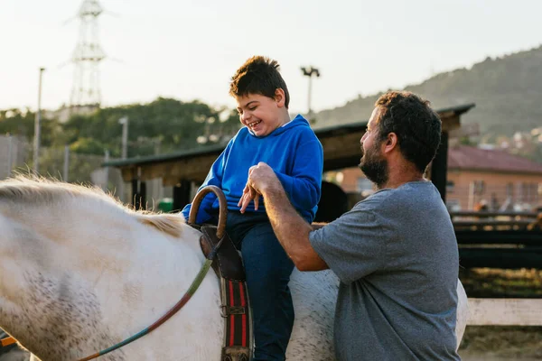 Smiley boy with cerebral palsy receiving equine therapy next to a physiotherapist in a ranch