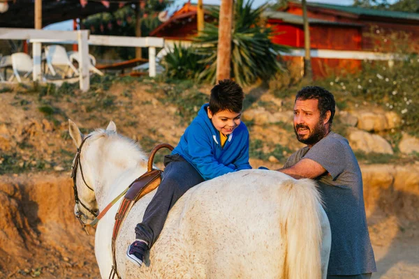 Physiotherapist during an equine therapy session using a white horse riding by a disabled child