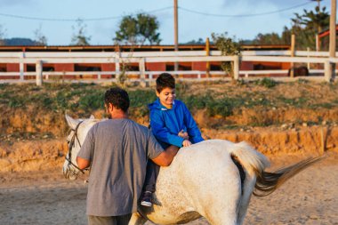 Man assisting a child with disabilities in an assisted equine therapy session. People with disabilities.