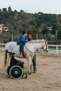 Boy with disabilities having his equine therapy with an instructor. Equine therapy concept.