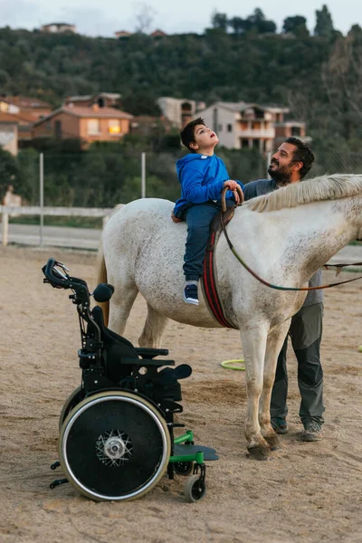 Boy with disabilities sitting on a horse while having his equine therapy. Equine therapy concept.