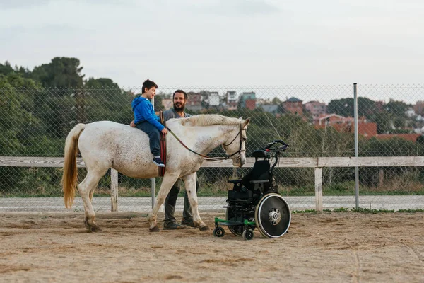 Boy with disabilities riding a horse while having an equine therapy session with an instructor. Equine therapy concept.
