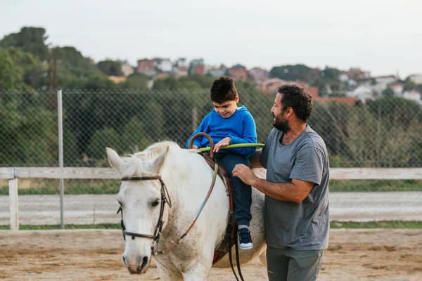Boy with disabilities exercising on a horse during an equine therapy session. Equine therapy concept.