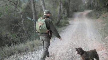 Erkek avcı, köpeğiyle ormanda yürürken silah tutuyor. Avlanma kavramı.