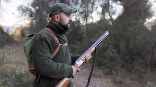 ハンターの男は銃を持ち 自然の中で獲物を探しながら周りを見回します 狩猟シーズンのコンセプト — ストック動画