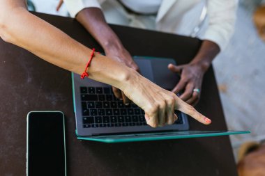 Beyaz bir kadın ekranı işaret ederken, Afro-Amerikalı bir kadının laptopunda yazı yazışının hava görüntüsü. Bir yandan cep telefonları var ve bir kafede oturuyorlar.