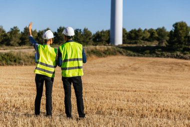 Rüzgâr türbini çiftliğinde çalışan üniformalı profesyonel mühendisler. Mühendislik, yenilenebilir enerji ve sanayi konsepti.