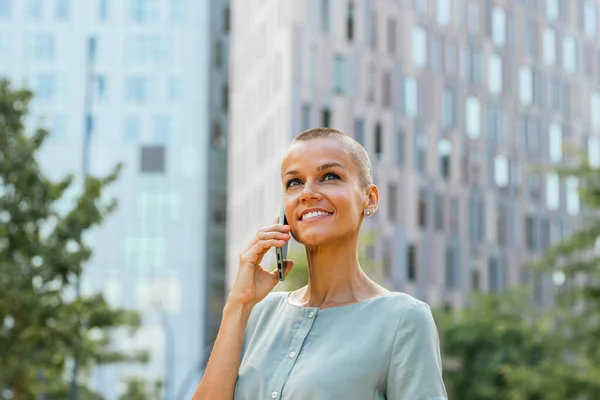 stock image a confident and cheerful 40-year-old woman with short hair. With a smile on her face, she looks upwards, creating ample copy space for advertising purposes. In her hand, she holds a smartphone and