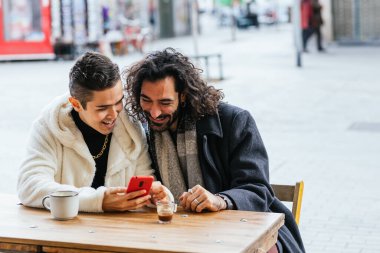 Restoranda oturmuş cep telefonu ekranlarına bakarak şehirde güzel vakit geçiren gülümseyen bir çift..