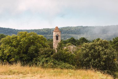 Tarragona, Katalonya, İspanya 'da bulunan La Mussara Dağı' nın tepesinde, yıkıntılar içindeki Romen tarzı kilise, ağaçlar ve çalıların arasında. Bir yaz günü, sisli