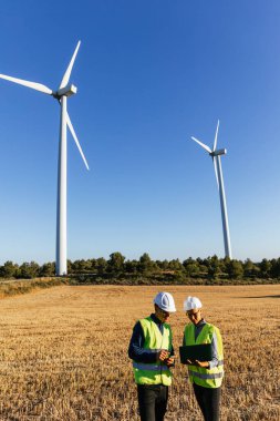 Yel değirmeni tarlasında dizüstü bilgisayarla çalışan mühendisler, temiz ve yenilenebilir enerji üretimi üzerinde çalışıyorlar..