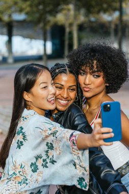 Mutlu çoklu etnik kadın ve transseksüel kadının birlikte selfie çekerken çekilmiş dikey fotoğrafı.
