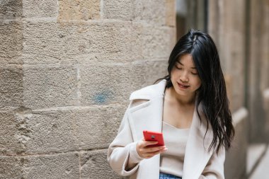 Dışarıda cep telefonunu kullanırken gülümseyen Asyalı bir kadın. Teknoloji konsepti.